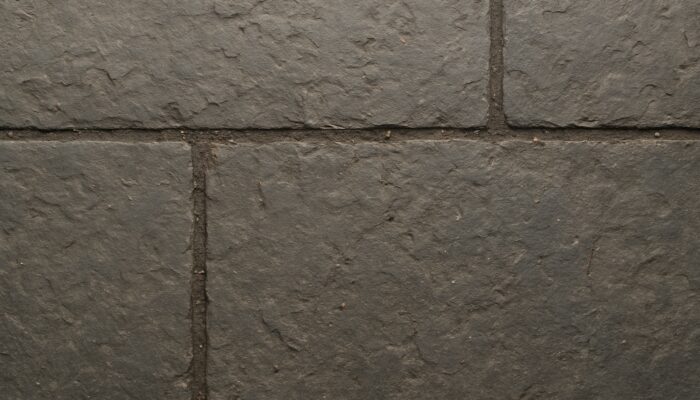 Close-up of worn pitted slate kitchen floor trapping dirt in riven texture with darkened grout lines